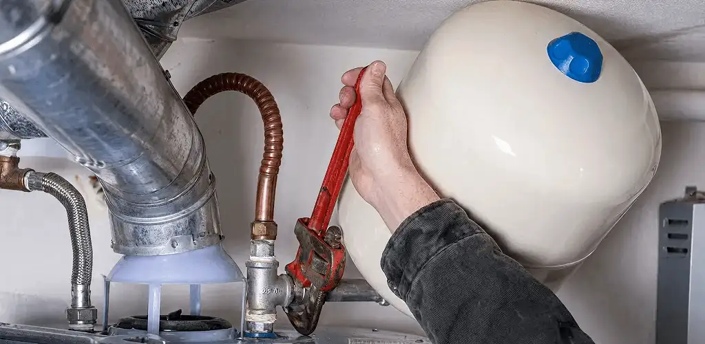 Water heater repair technician tightening plumbing connections near a tank unit in West Palm Beach, FL